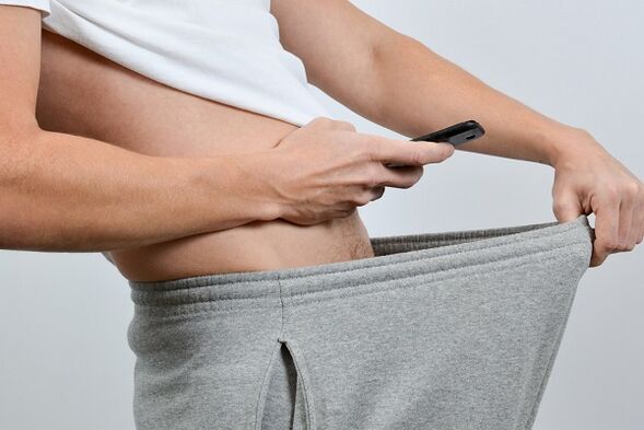 un hombre mira debajo de sus pantalones un pene agrandado